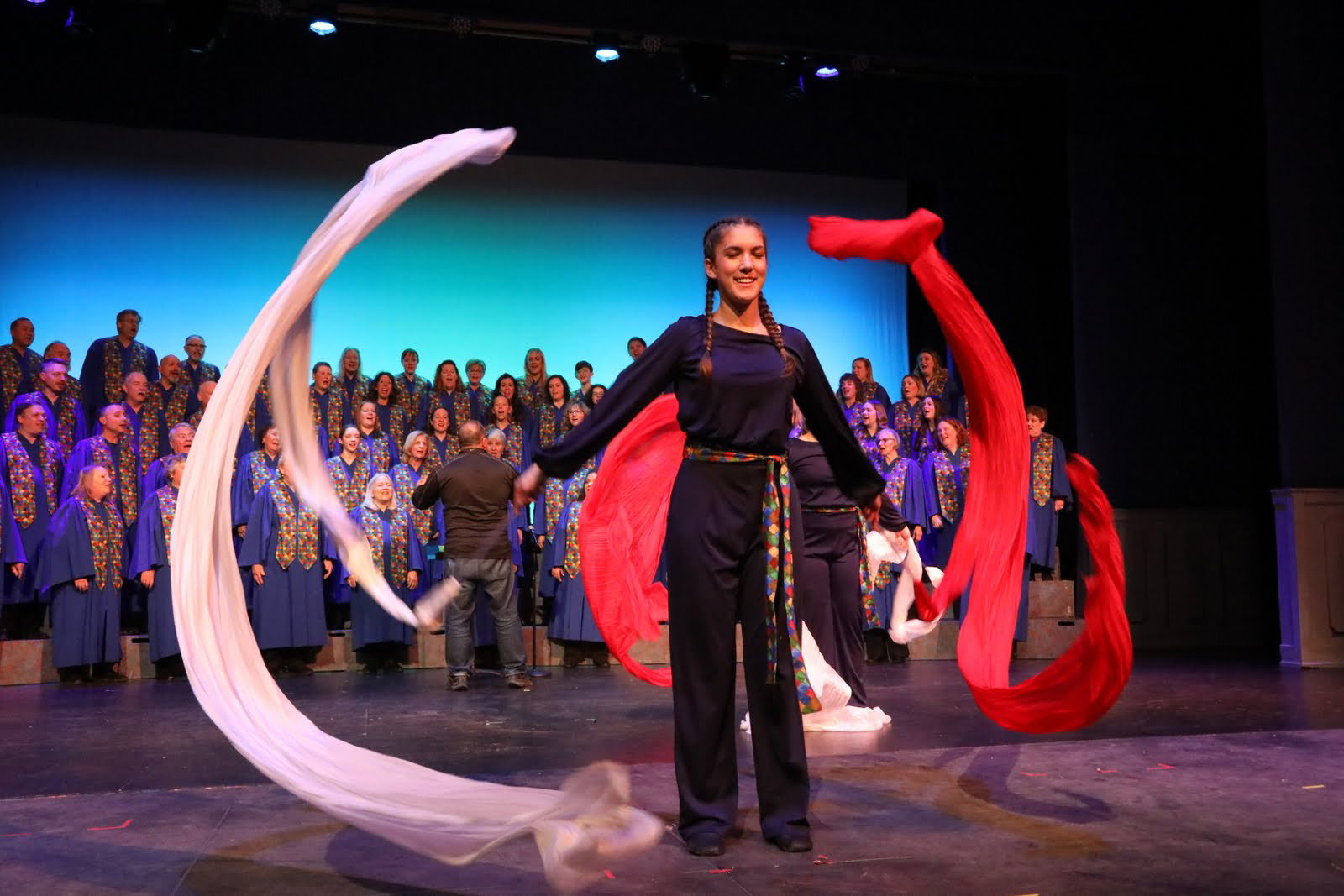 A dancer twirls scarves with an adult choir in the background.